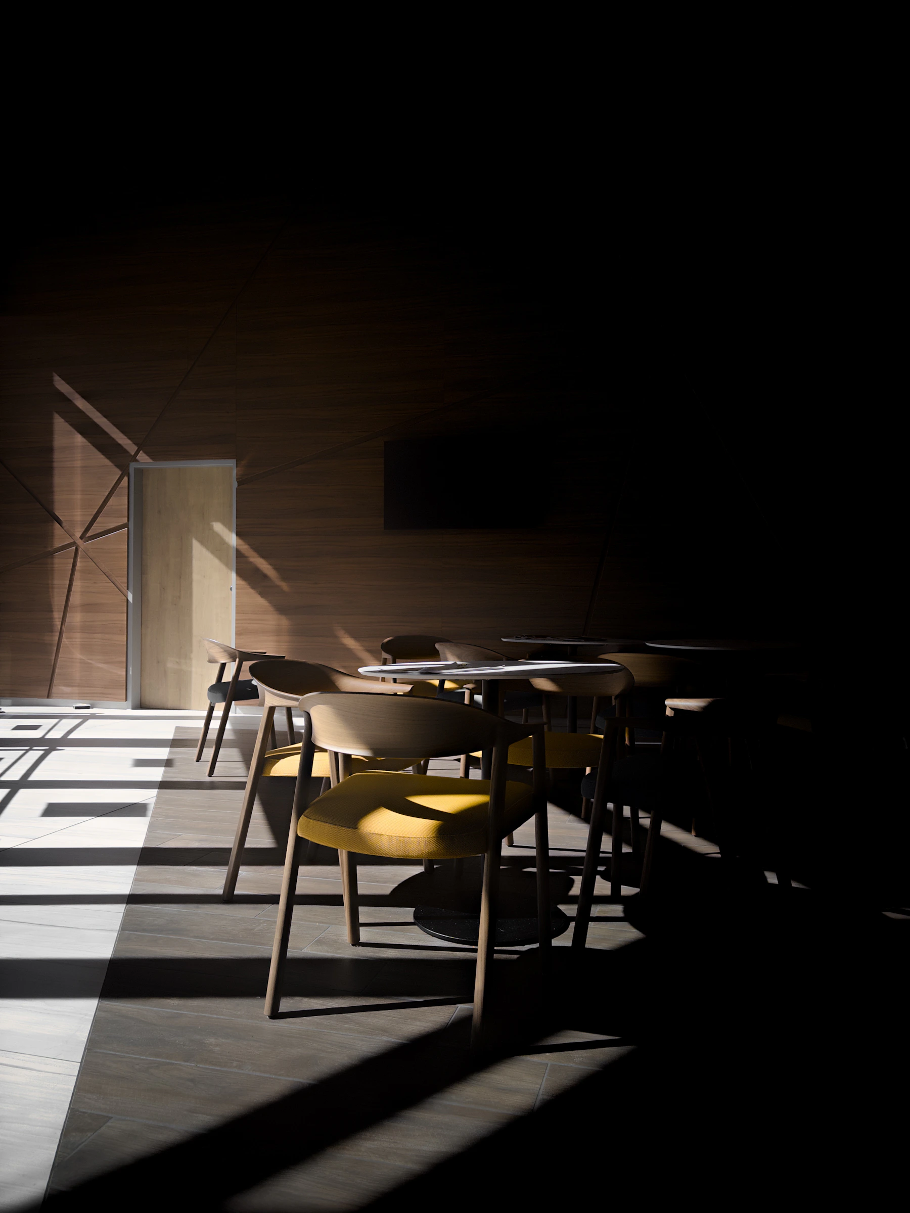 Light falling across a quiet modernist interior with walnut chairs